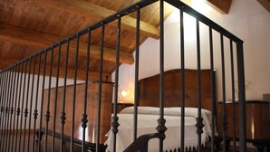 Una escalera de madera con barandal negro que lleva a un dormitorio con cama y mesita de noche.