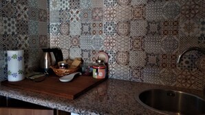 Una cocina con baldosas estampadas, un lavamanos de acero inoxidable y diferentes utensilios de cocina sobre la encimera.