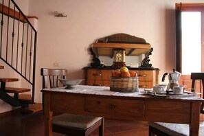 A kitchen with a wooden table, a fruit basket, a coffee maker, and a chair.