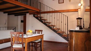 Un amplio salón con una escalera de madera, una mesa de comedor con sillas y una pequeña mesita de noche con lámpara.