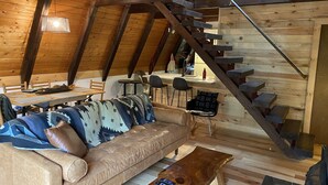 Une pièce confortable de style loft, avec un plafond en bois, un canapé, une table basse, un bureau et un escalier.