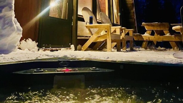 Une cabane en bois avec une façade en verre, une terrasse en bois et un sol recouvert de neige.