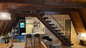 Un espace de vie chaleureux de style loft, doté d’un escalier en bois, d’un coin cuisine et d’un espace détente avec un canapé et des fauteuils.