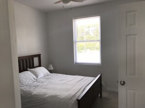 Un dormitorio con una cama individual, una mesita de noche, una lámpara y una ventana con persianas.