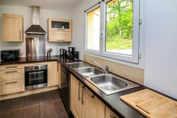 Una cocina moderna con electrodomésticos de acero inoxidable, armarios de madera y un amplio ventanal con vistas a zonas verdes.