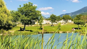 A serene lakeside view with grassy areas, trees, and a clear sky. - Deluxe villa with private pool and beautiful mountain view (Malaucène)