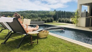 A person relaxing by a poolside with a book, a small table with a basket, and a kayak in the water. - Deluxe villa with private pool and beautiful mountain view (Malaucène)