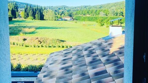 A view from a window overlooking a green landscape with a house and a small structure with a solar panel. - Deluxe villa with private pool and beautiful mountain view (Malaucène)