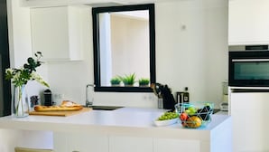 A modern kitchen with a central island, bar stools, a window with plants, and a built-in oven. - Deluxe villa with private pool and beautiful mountain view (Malaucène)