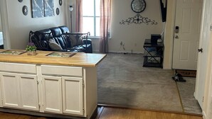 Una sala de estar con piso de madera, un sofá de cuero negro, un armario blanco y un comedor con mesa de madera.