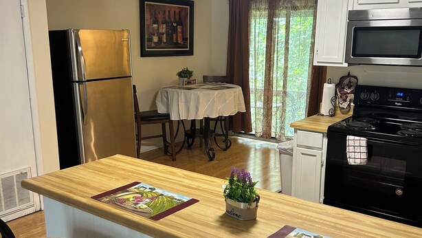 Una cocina con una isla de madera, dos taburetes de bar, un refrigerador, un microondas y una estufa.