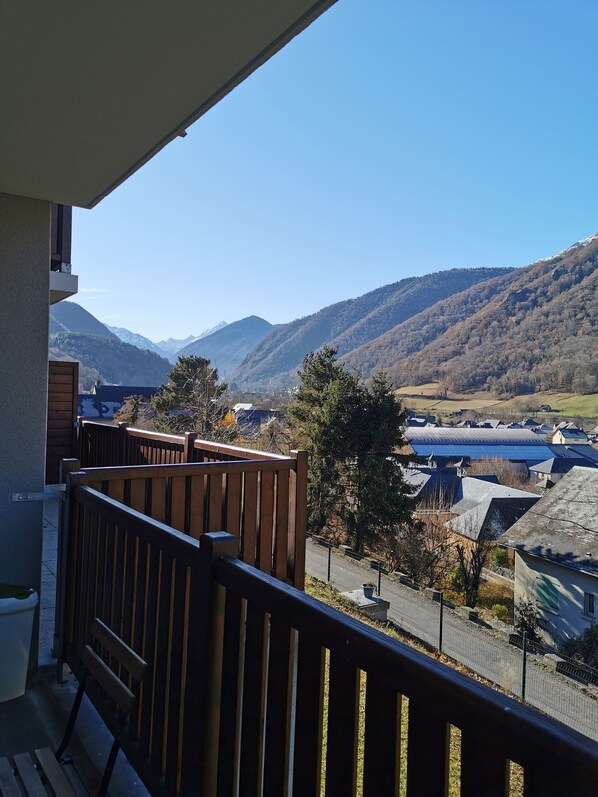 A balcony with a view of a mountainous landscape, a wooden fence, and a clear sky.