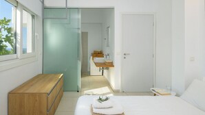 Ein modernes Schlafzimmer mit einem Holzkapfen, einem Bett mit Handtuch und Buch, einem Badezimmer mit Waschbecken und Spiegel sowie einer Tür zu einem weiteren Raum.