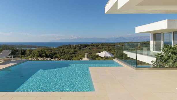 Ein moderner Poolbereich mit freiem Blick auf das Meer und die dahinterliegenden Berge.