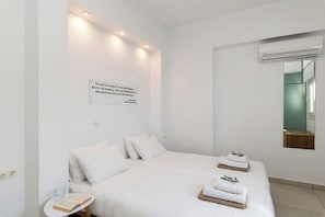 A modern hotel room with a large bed, white bedding, a bedside table with a book and glass, and a wall-mounted air conditioning unit.