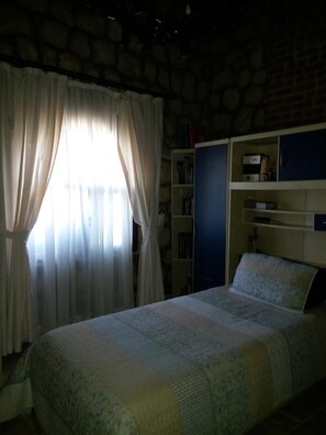 Ein Schlafzimmer mit einem Bett, einem Bücherregal und einem Fenster mit Vorhängen.