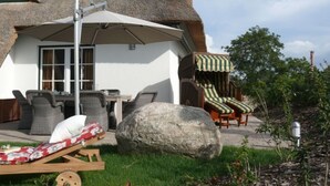 A thatched-roof house with outdoor seating, including a table and chairs, and a large rock in the foreground. - Reethus, 3 bedrooms + 1 infant, 2 bathrooms, fireplace, sauna, outdoor whirlpool, garden, WLAN (Seebad Heringsdorf)