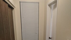 A narrow hallway with a wooden floor, a window with blinds, and a white door. - Apartment in The Historical Stahl House Building. (Mankato)