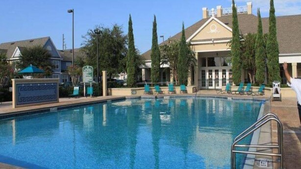 A swimming pool with lounge chairs and a building with a sign in the background. - Perfect Family Vacation Spot close to major Orlando attractions! (Kissimmee)