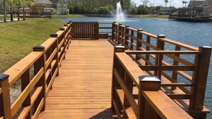 A wooden boardwalk leading to a body of water with a fountain, surrounded by grassy areas and residential buildings. - Perfect Family Vacation Spot close to major Orlando attractions! (Kissimmee)