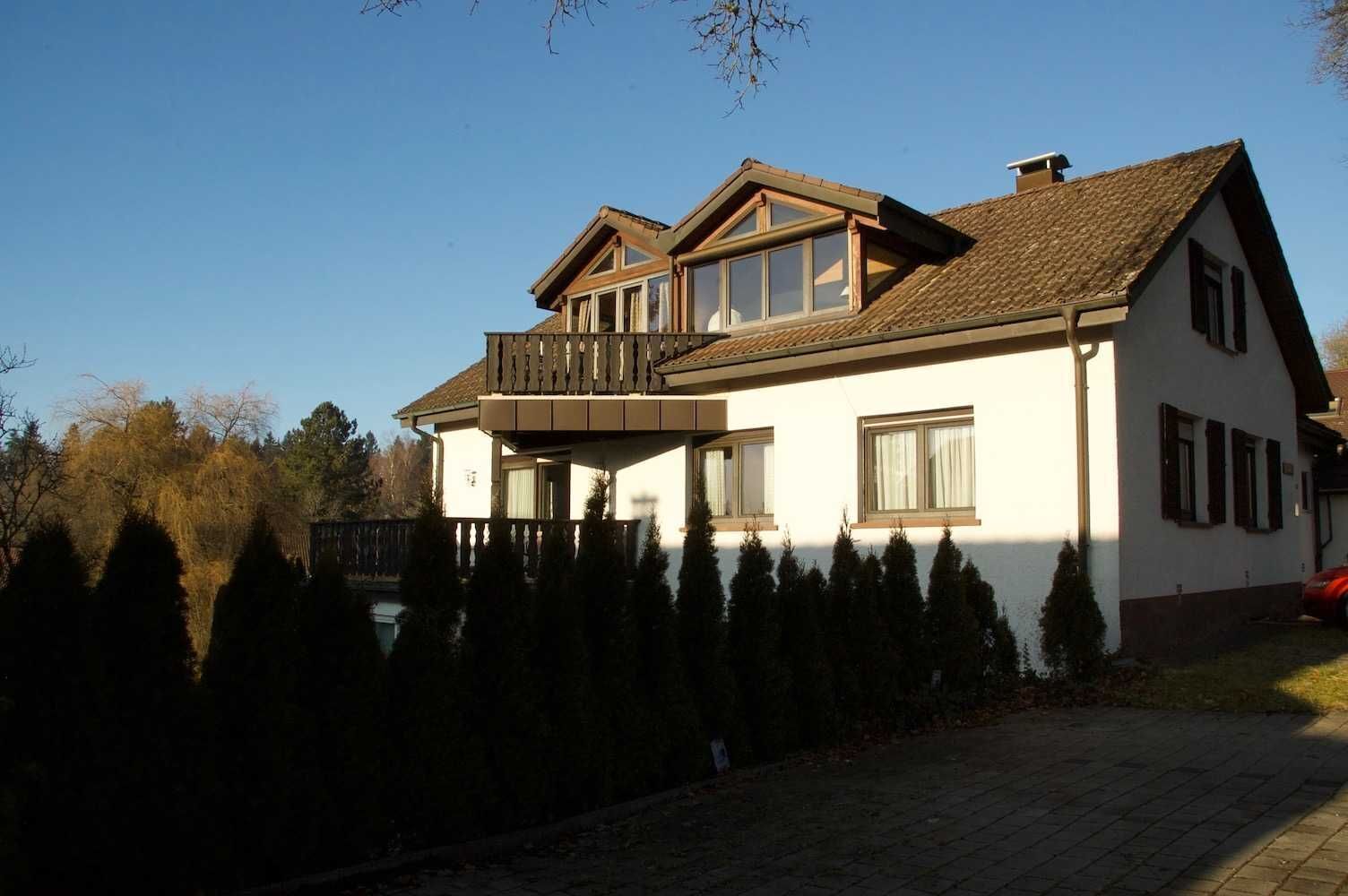 Ein zweigeschossiges Haus mit Balkon, großen Fenstern und einem Ziegelweg.