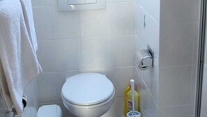 Un baño con un inodoro, un cubo de basura, un dispensador de papel higiénico y una botella de limpiador.