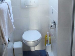 Une salle de bain équipée de toilettes, d’une poubelle, d’un porte-rouleau de papier toilette et d’un vaporisateur de produit nettoyant.