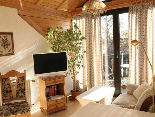 Un salon confortable avec une télévision, une bibliothèque, une plante en pot, un canapé et une table.