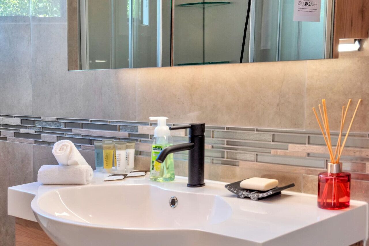 A modern bathroom with a white sink, a black faucet, a glass mirror, and a tiled backsplash.
