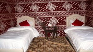 Una habitación con dos camas, cada una con ropa de cama blanca y almohadas rojas, una mesita con un objeto decorativo y una pared con estampado.