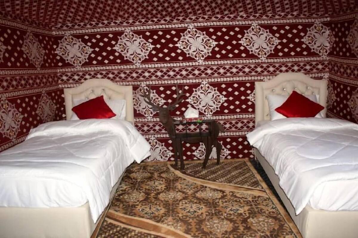 Une chambre avec deux lits, chacun agrémenté de draps blancs et d’oreillers rouges, une petite table sur laquelle est posé un objet décoratif, et un mur orné d’un motif.