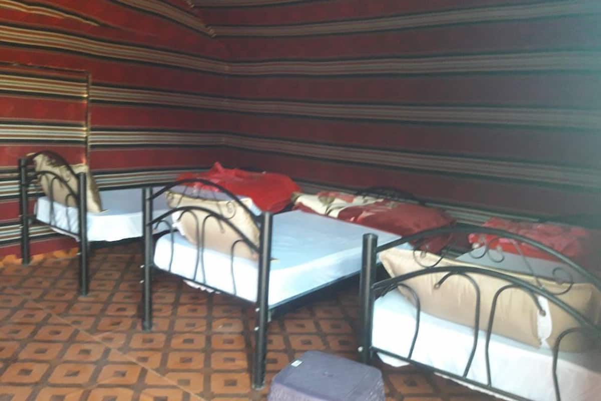 Une pièce avec trois lits superposés en métal, chacun étant équipé d’un matelas et d’oreillers. La pièce a un sol à motifs et des murs rayés.