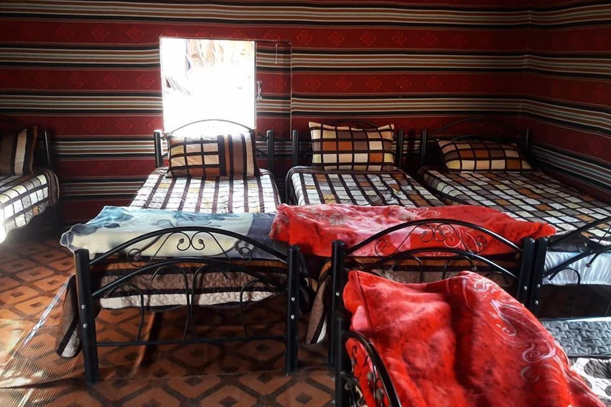 Une pièce avec quatre lits disposés en carré, chacun étant agrémenté d’une couvre-lit et de coussins à motifs. Une fenêtre située au centre permet à la lumière naturelle d’entrer.