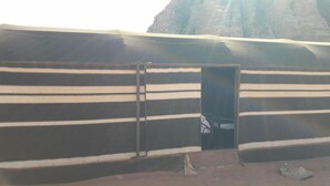 Una gran puerta metálica a rayas con una puerta pequeña, ubicada frente a un paisaje desértico con un risco rocoso.