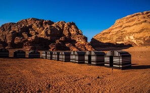 A desert landscape with rock formations and a row of striped tents.