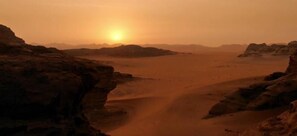 A desert landscape with a clear sky and a sun setting or rising.