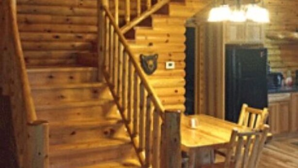 A log cabin interior with a wooden staircase, a dining area with a table and chairs, and a fireplace. - Lazy Cedars Log Cabin - Centrally located (Blaney Park)