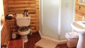 A wooden cabin bathroom with a toilet, a shower enclosure, and a sink. - Lazy Cedars Log Cabin - Centrally located (Blaney Park)
