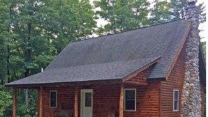 A log cabin with a porch, a stone chimney, and a small front door. - Lazy Cedars Log Cabin - Centrally located (Blaney Park)
