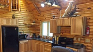 A log cabin interior with a kitchen area, a refrigerator, a stove, and a chair. - Lazy Cedars Log Cabin - Centrally located (Blaney Park)