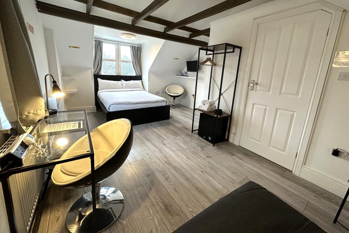A modern bedroom with a bed, a desk with a chair, a bedside table, a hanging shelf, and a wardrobe.