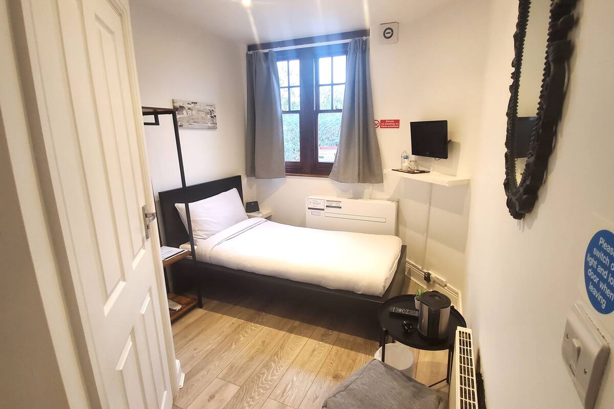A compact bedroom with a bed, bedside table, TV, and a window with curtains.