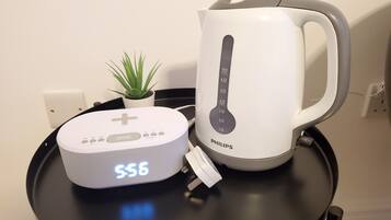 A white Philips kettle, a white speaker with a digital display, and a small green plant on a black table.