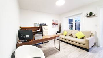 A modern office space with a desk, computer, and filing cabinet. There is a sofa with cushions and a window with blinds.
