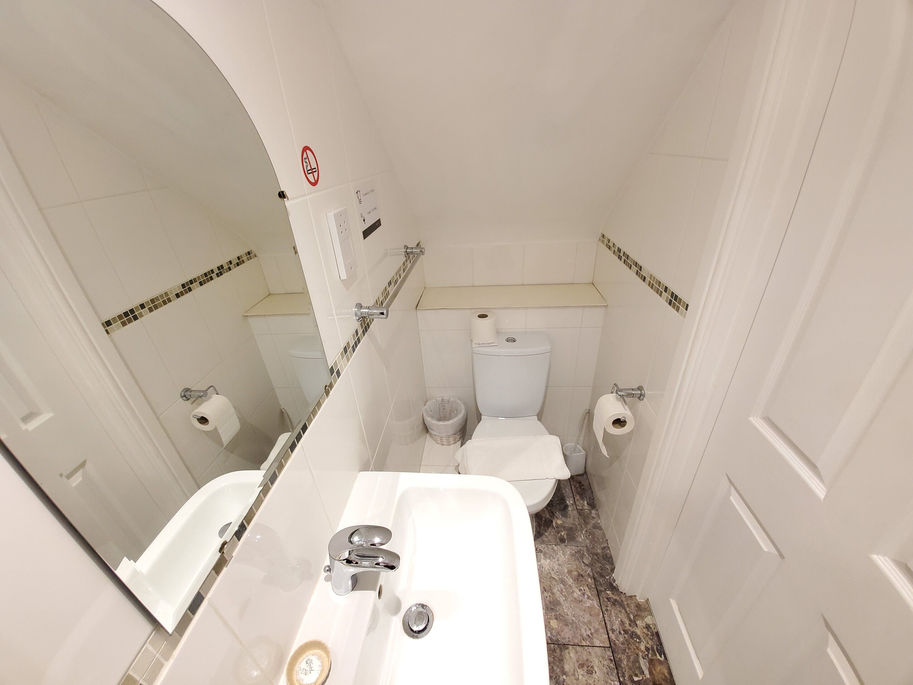 Un baño pequeño y estrecho con un lavamanos blanco, un inodoro y un espejo.