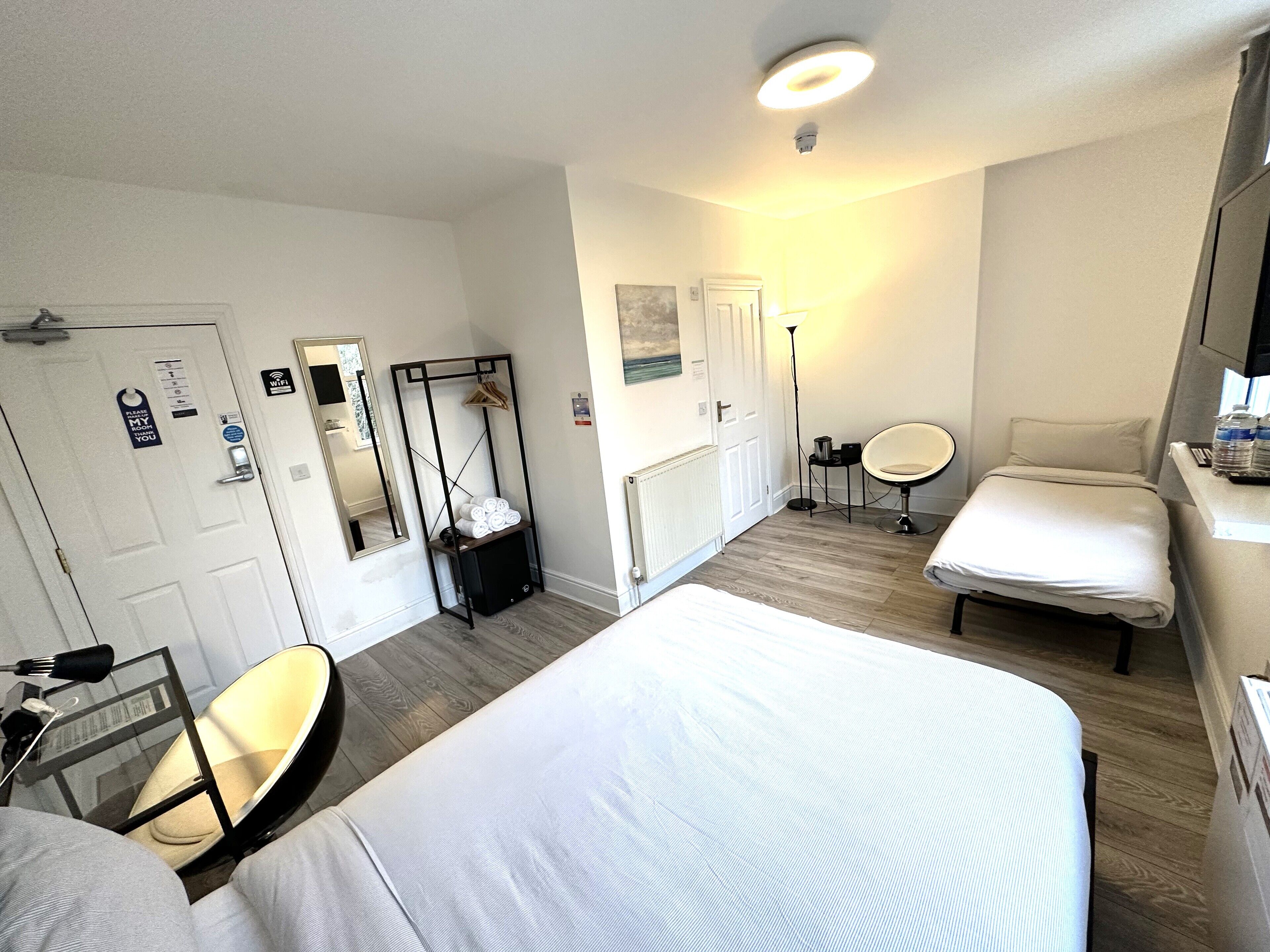 A hotel room with two beds, a mirror, a wardrobe, a desk with a chair, a floor lamp, and a small table.