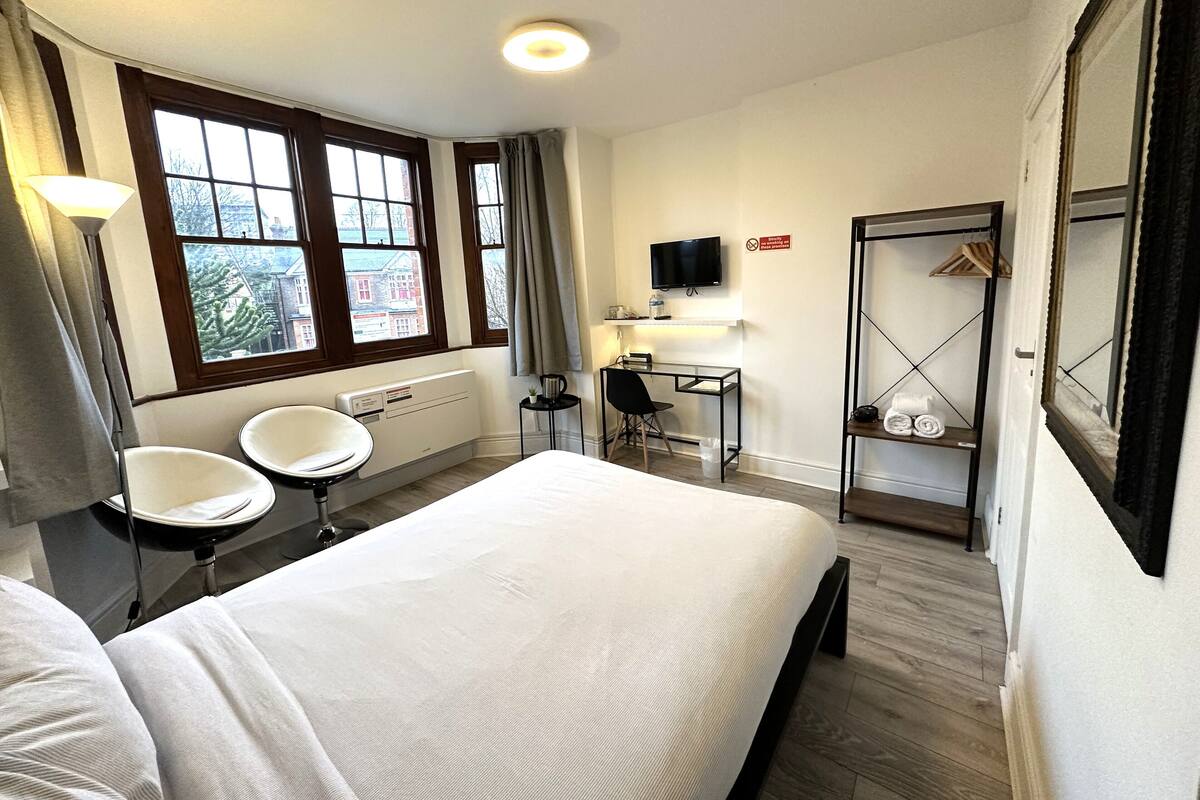 A hotel room with a bed, a desk, a chair, a TV, and a wardrobe.