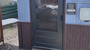 En dörr med en välkomstmatta, en skylt som visar ingången till Smith River Gateway Apartment, och ett litet förråd i bakgrunden.