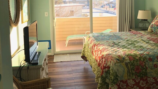 A bedroom with a bed, a desk with a computer, a chair, a ceiling fan, and a view of the outside. - The Pink Palace - Fenwick Island Beach Block w/ Pool & Super Easy Beach Access (Fenwick Island)