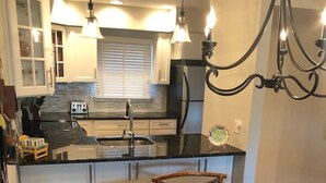 A kitchen with a central island, wooden chairs, a round glass table, and pendant lighting. - The Pink Palace - Fenwick Island Beach Block w/ Pool & Super Easy Beach Access (Fenwick Island)